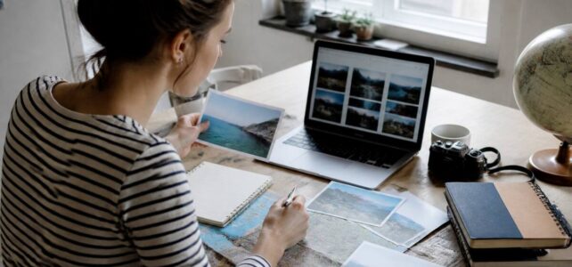 Iemand vergelijkt vakantieopties op een laptop met notities aan een keukentafel